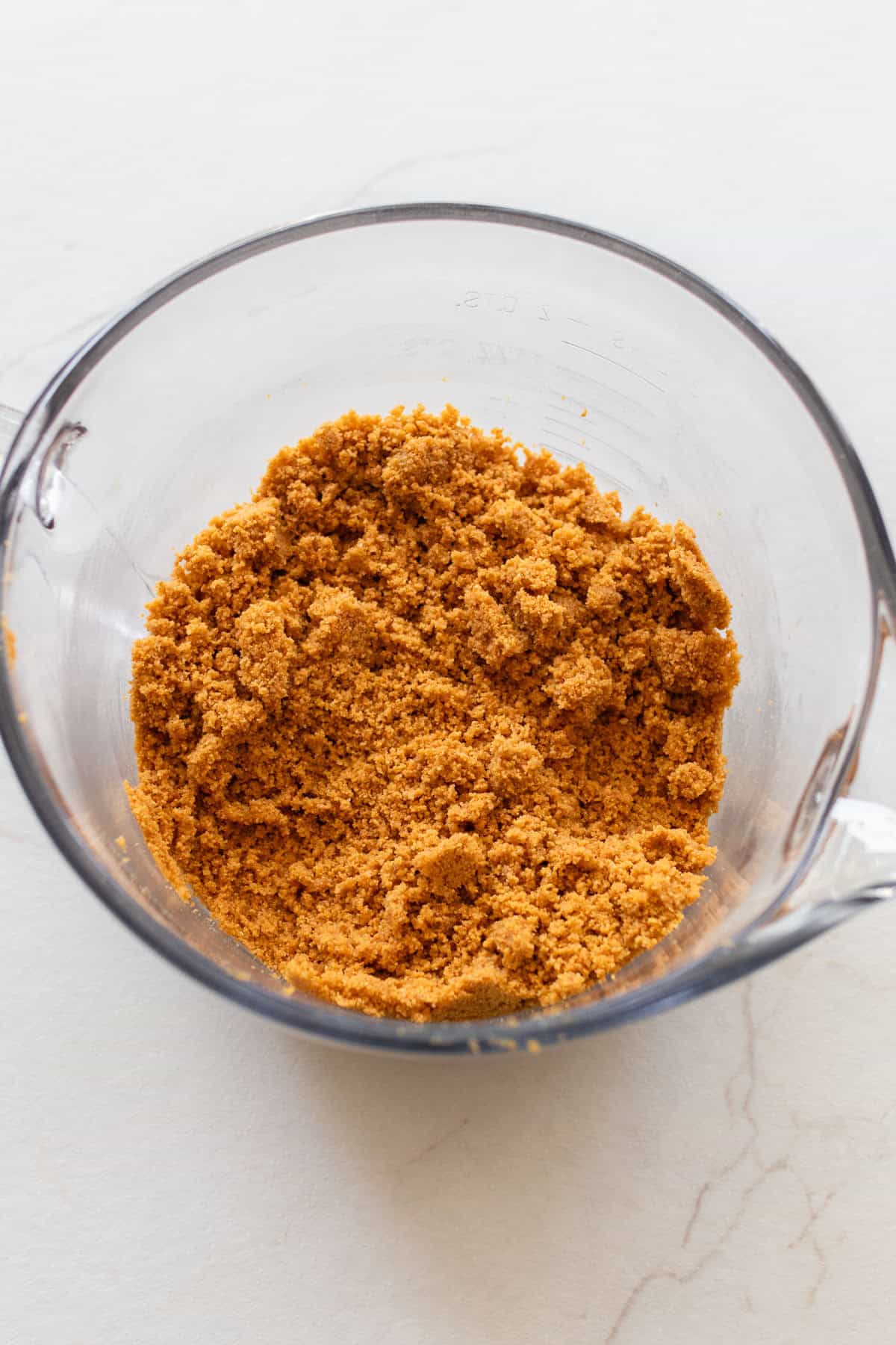 Graham cracker crumbs mixed with butter in a glass measuring bowl.