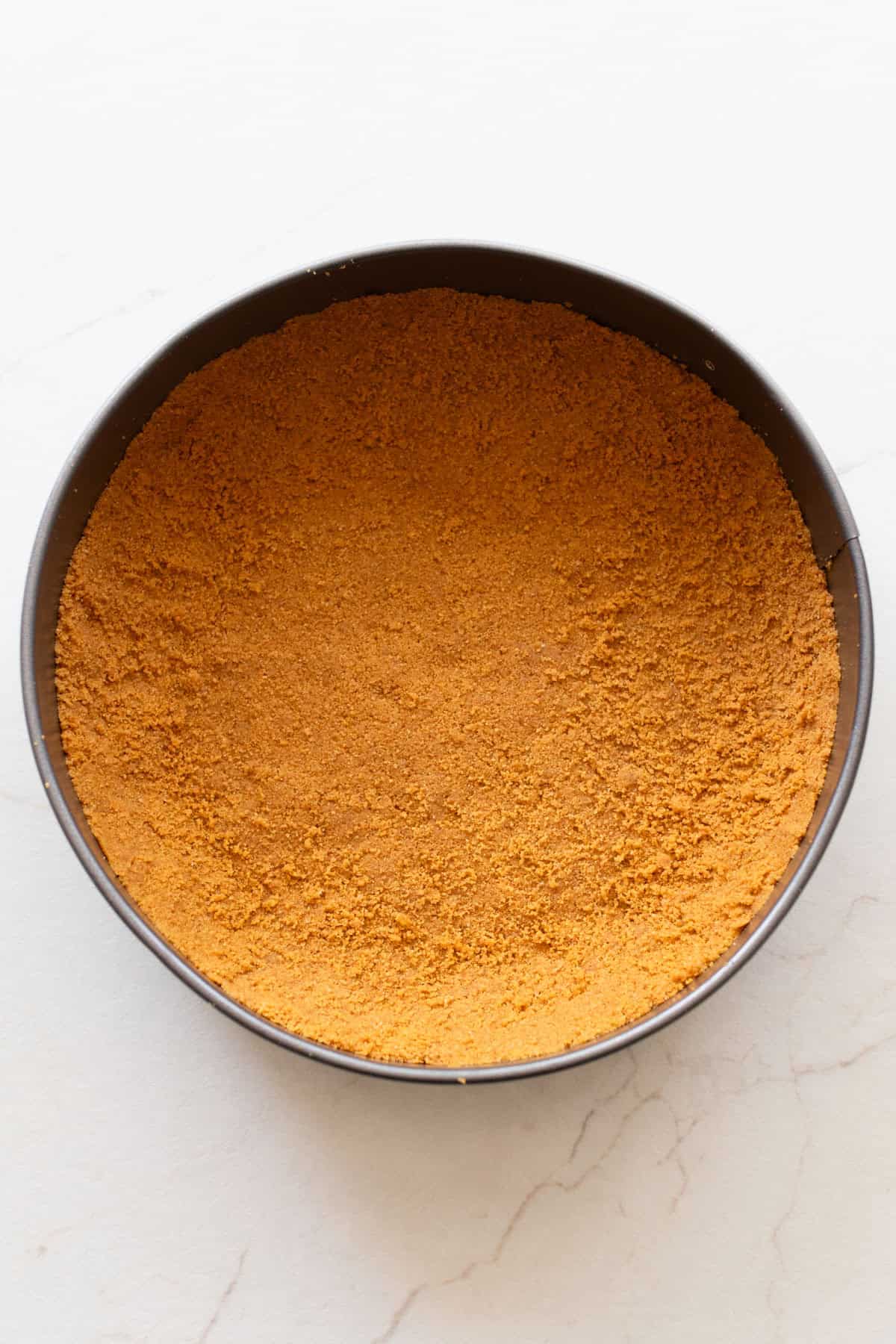 A springform pan with a graham cracker crust pressed into the bottom.