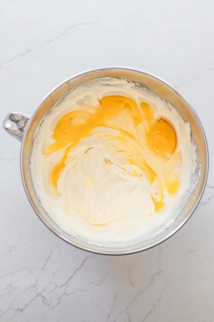 Egg yolks added to a whipped cream cheese mixture in a bowl.