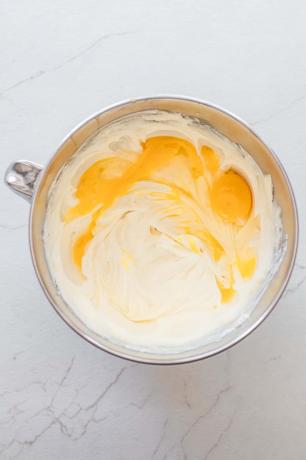 Egg yolks added to a whipped cream cheese mixture in a bowl.