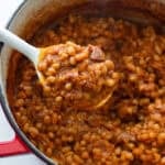 A spoon scooping baked beans out of a Dutch oven.