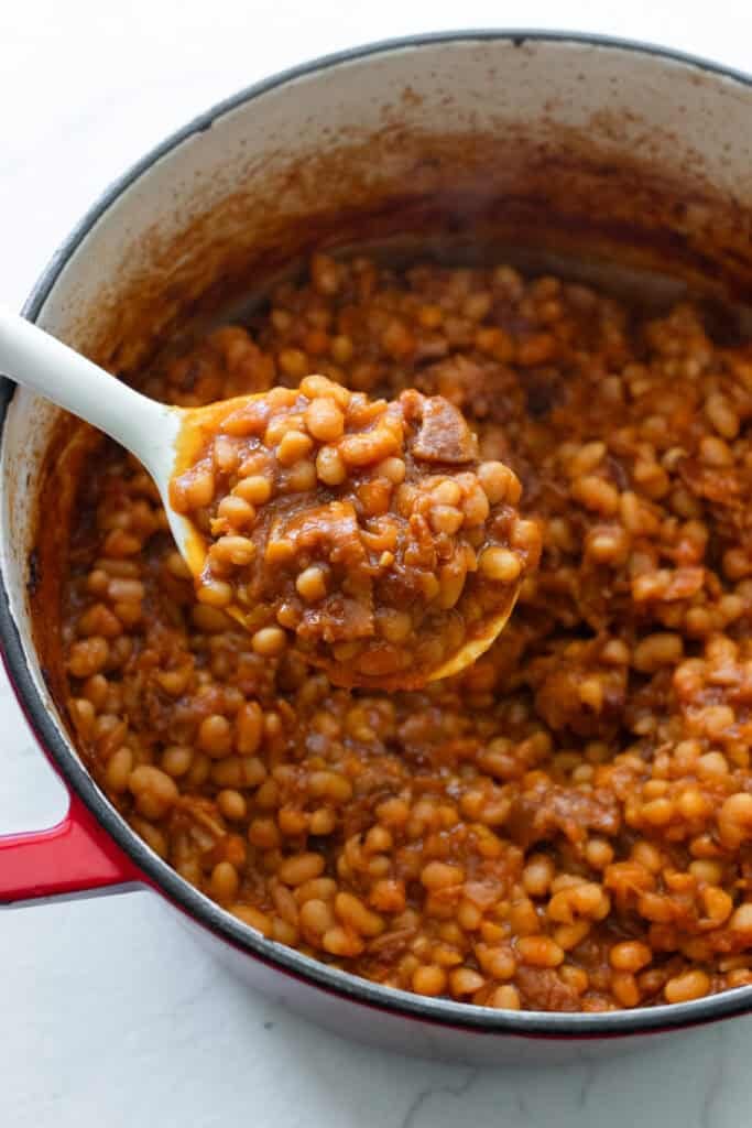 A spoon scooping baked beans out of a Dutch oven.