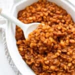 Baked beans in a white casserole dish with a spoon.