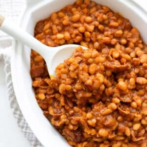 Baked beans in a white casserole dish with a spoon.
