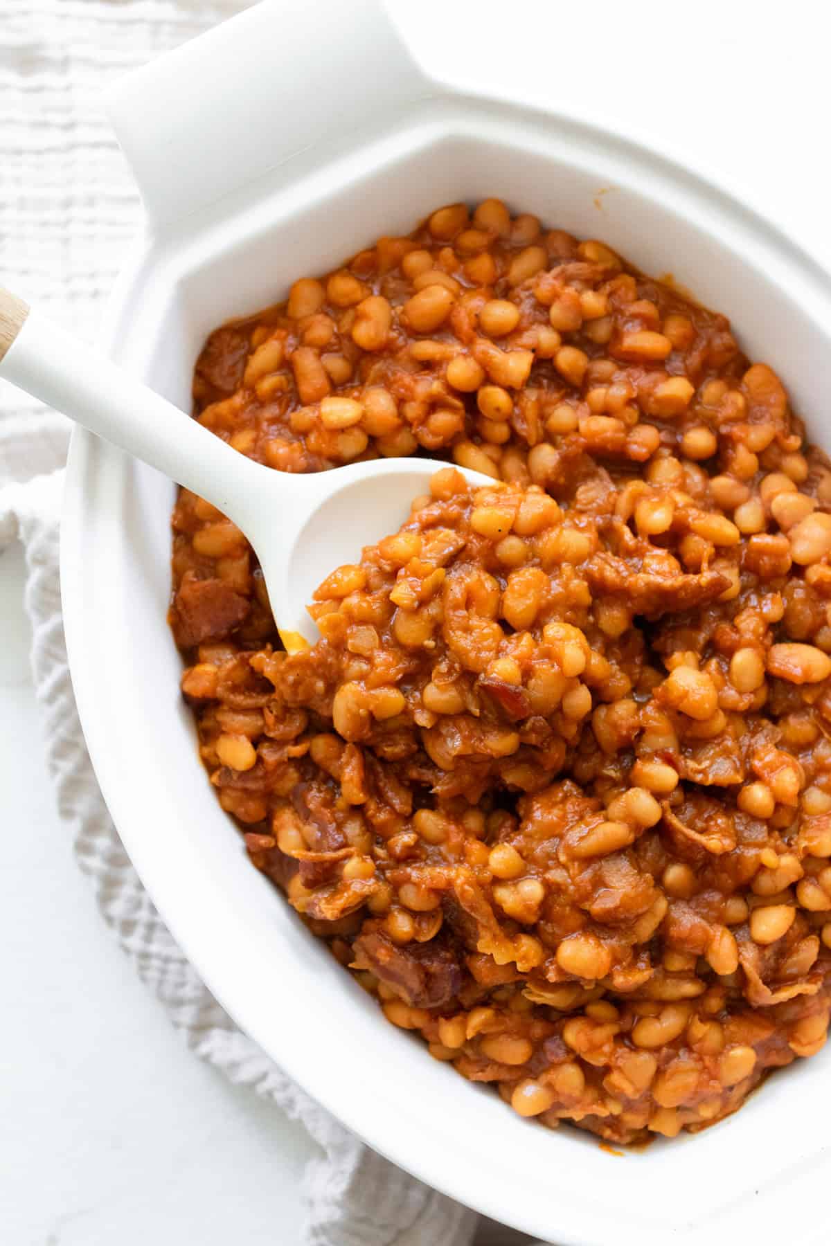 Baked beans in a white casserole dish with a spoon.