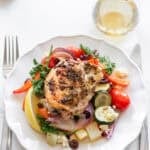 A plate with a chicken thigh and veggies and a knife and a fork on either side.