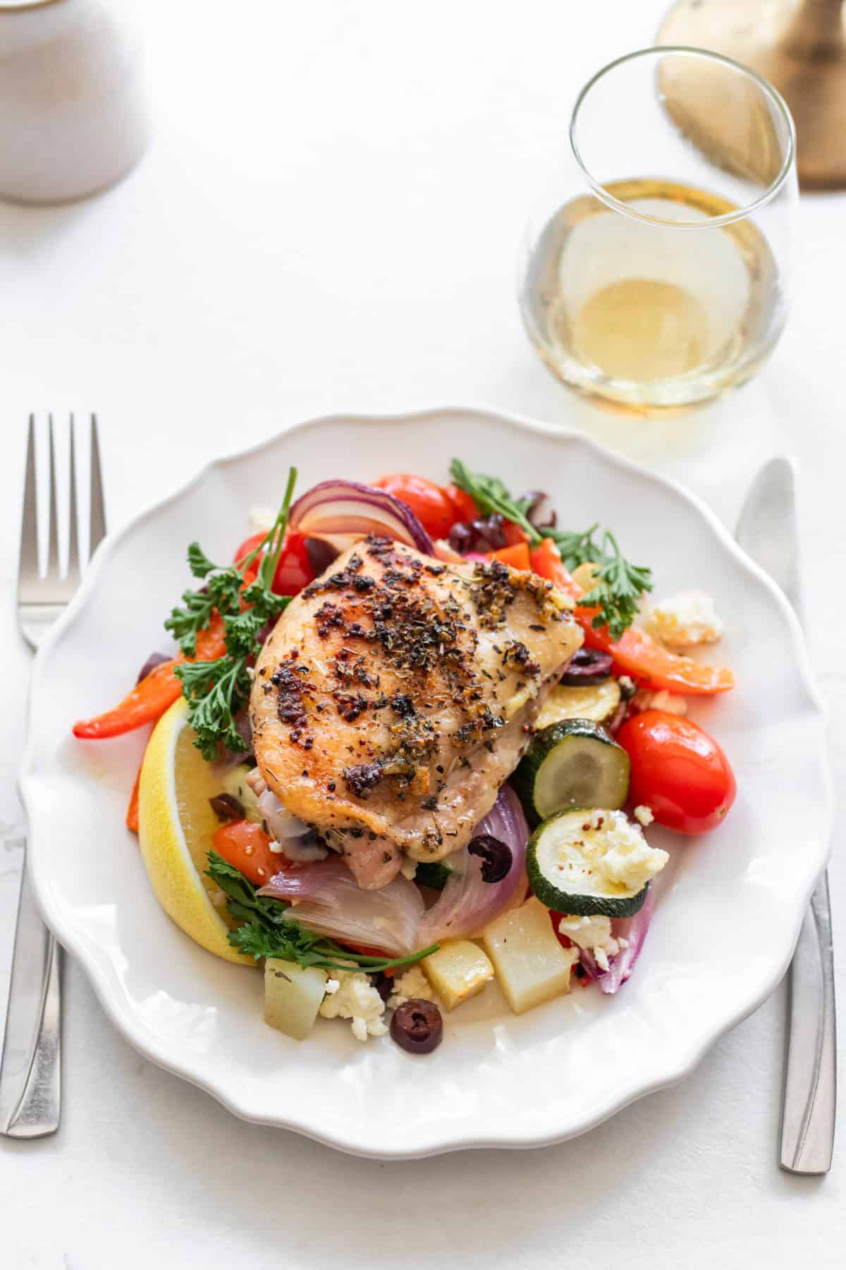 A plate with a chicken thigh and veggies and a knife and a fork on either side.