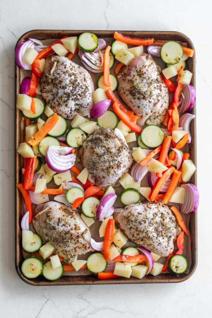 Chicken thighs surrounded by veggies on a sheet pan.
