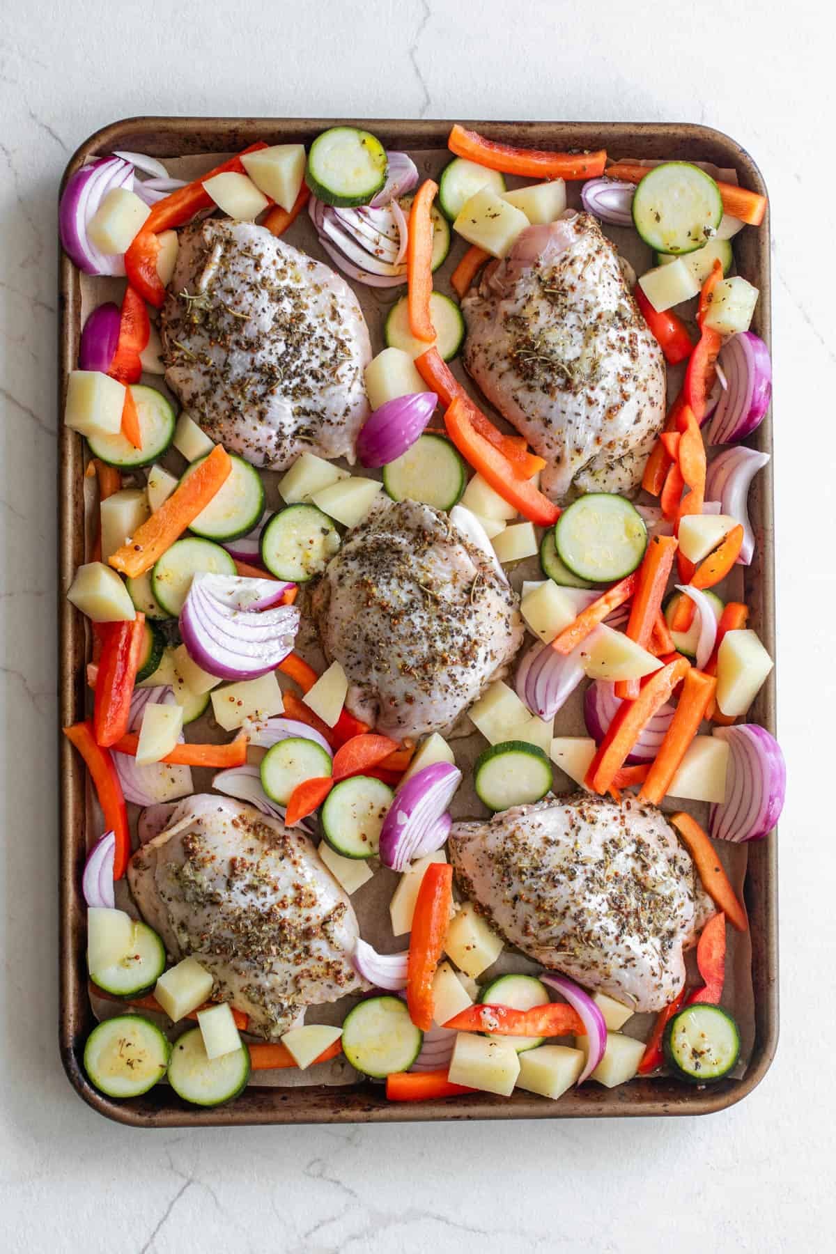 Chicken thighs surrounded by veggies on a sheet pan.