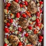 Cherry tomatoes added to a sheet pan of chicken thighs and veggies.