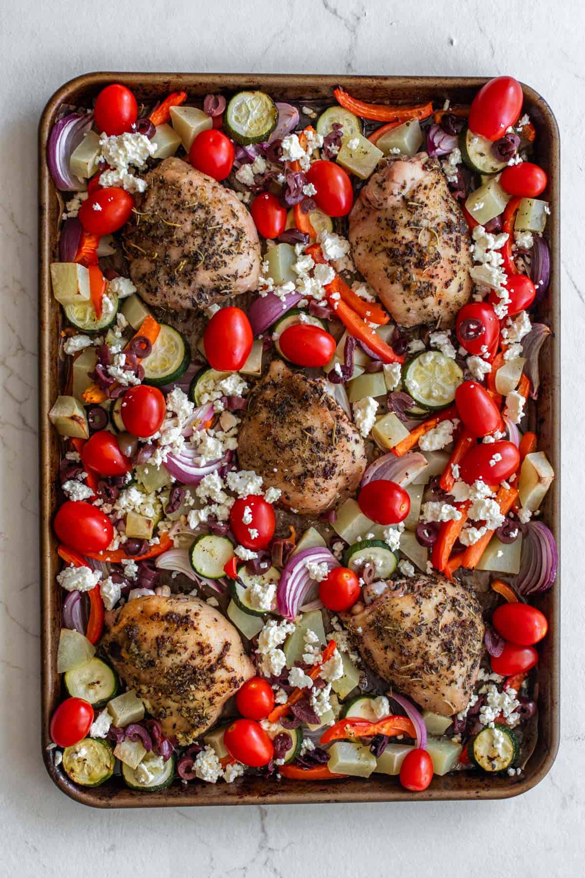 Cherry tomatoes and feta added to a sheet pan of chicken thighs and veggies.