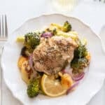 Chicken thigh on a plate surrounded by roasted veggies and gnocchi.