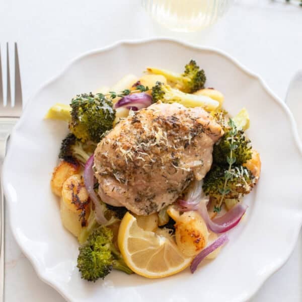 Chicken thigh on a plate surrounded by roasted veggies and gnocchi.