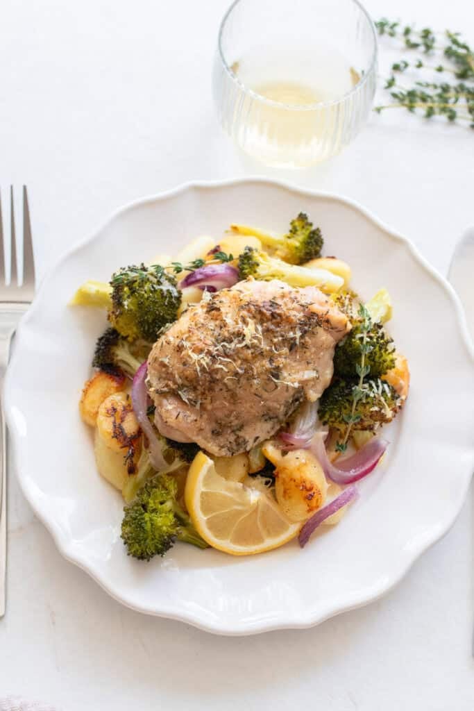 Chicken thigh on a plate surrounded by roasted veggies and gnocchi.