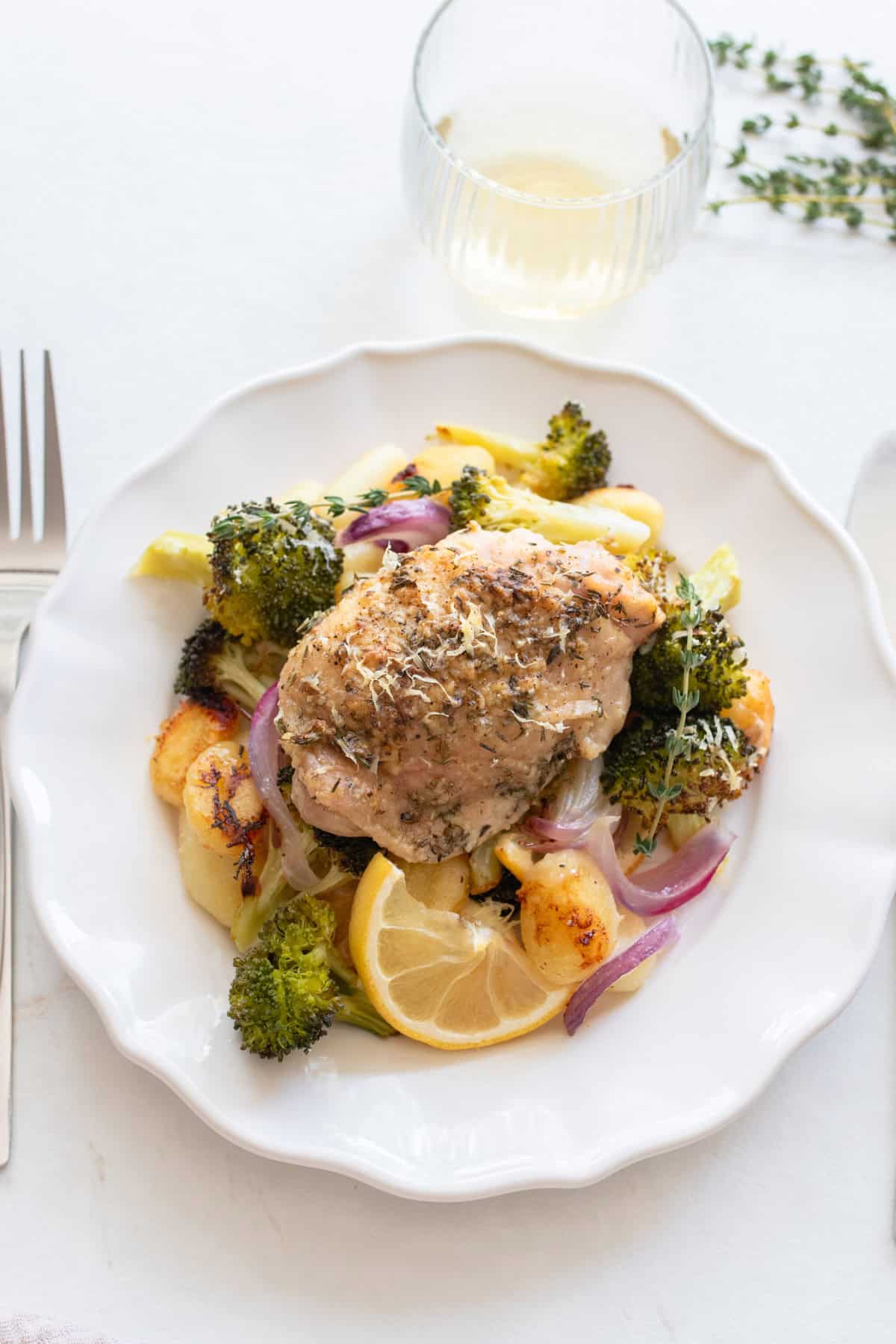 Chicken thigh on a plate surrounded by roasted veggies and gnocchi.