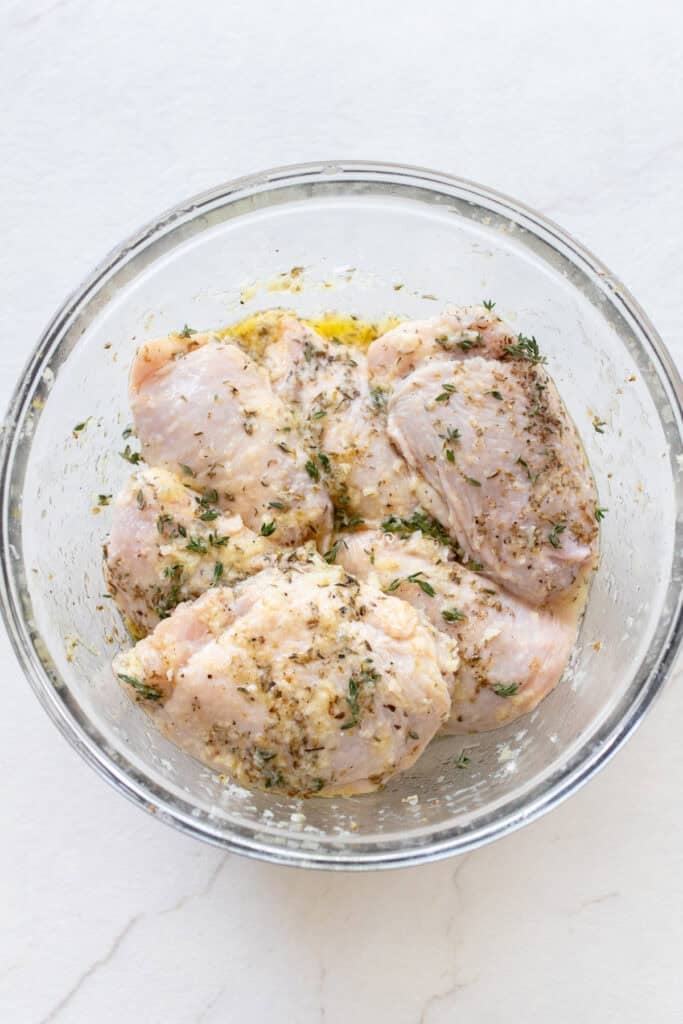 Chicken thighs in a marinade in a small glass bowl.