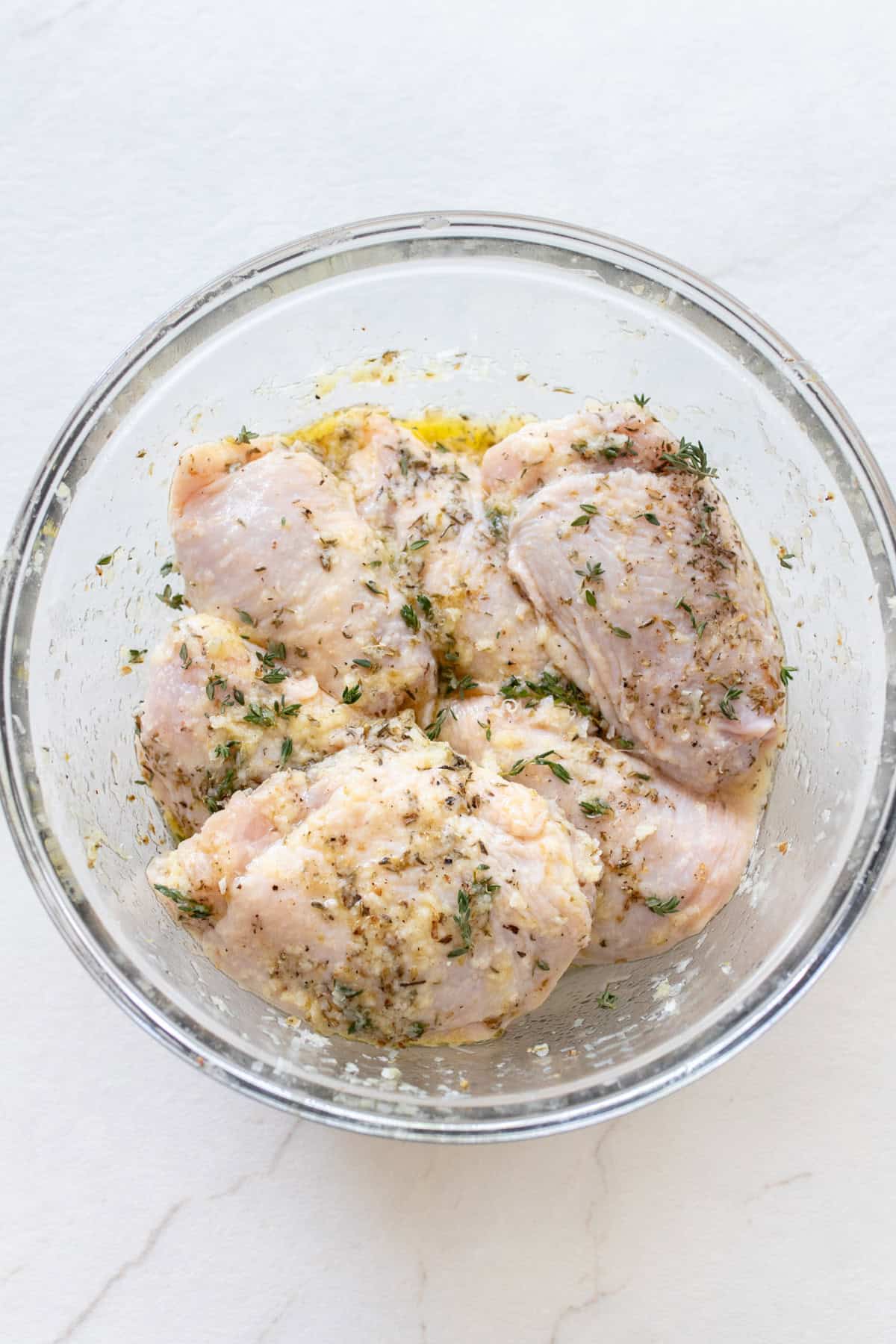 Chicken thighs in a marinade in a small glass bowl.