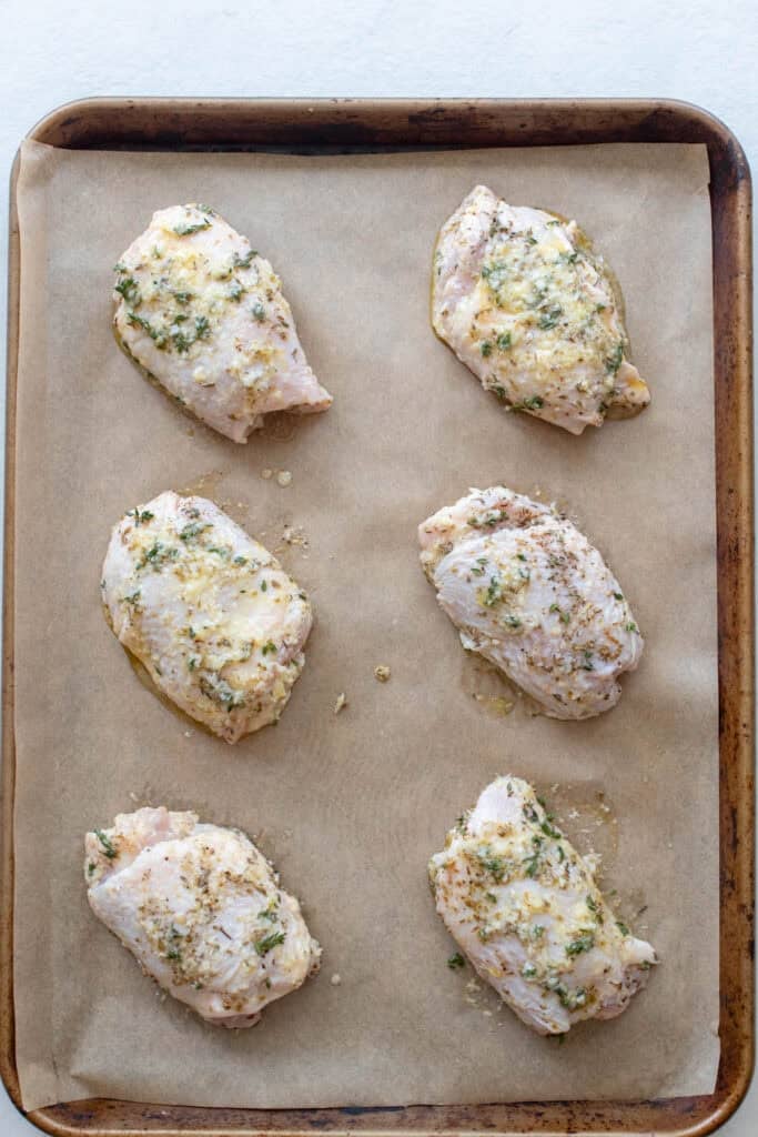 Chicken thighs on a sheet pan lined with parchment paper.