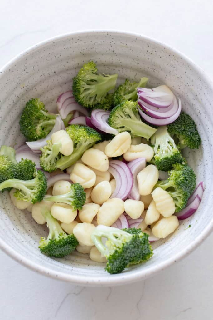Broccoli, onions, and gnocchi in a white bowl.