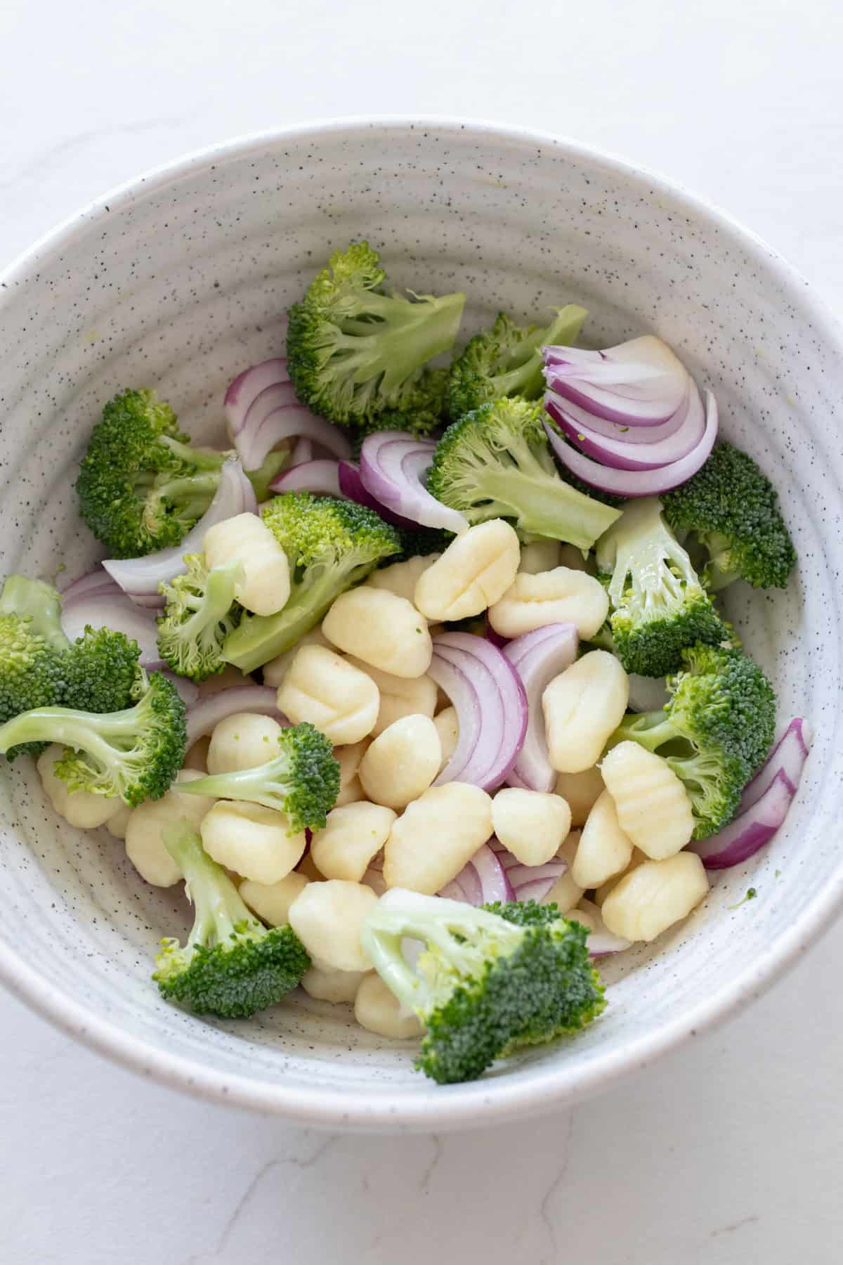 Broccoli, onions, and gnocchi in a white bowl.