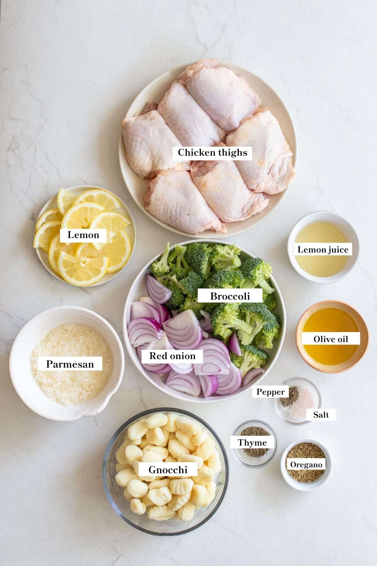 Ingredients for sheet pan gnocchi with chicken and vegetables in bowls on a white counter top.