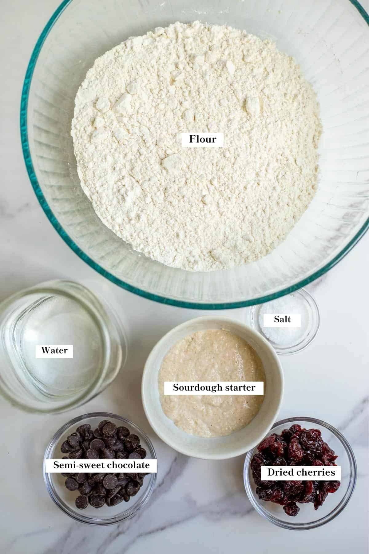 Ingredients for a chocolate cherry sourdough loaf on a marble counter top.