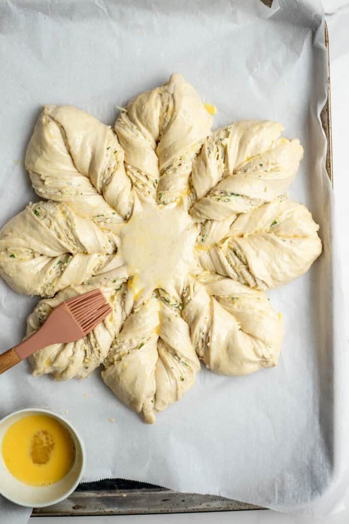 A rubber spatula coating the sourdough cheese star dough with an egg wash before baking.