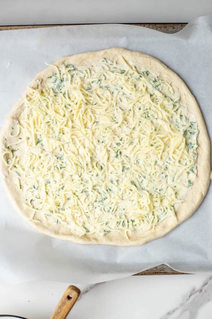 A circular shaped sourdough layer topped with garlic herb butter and shredded cheese.