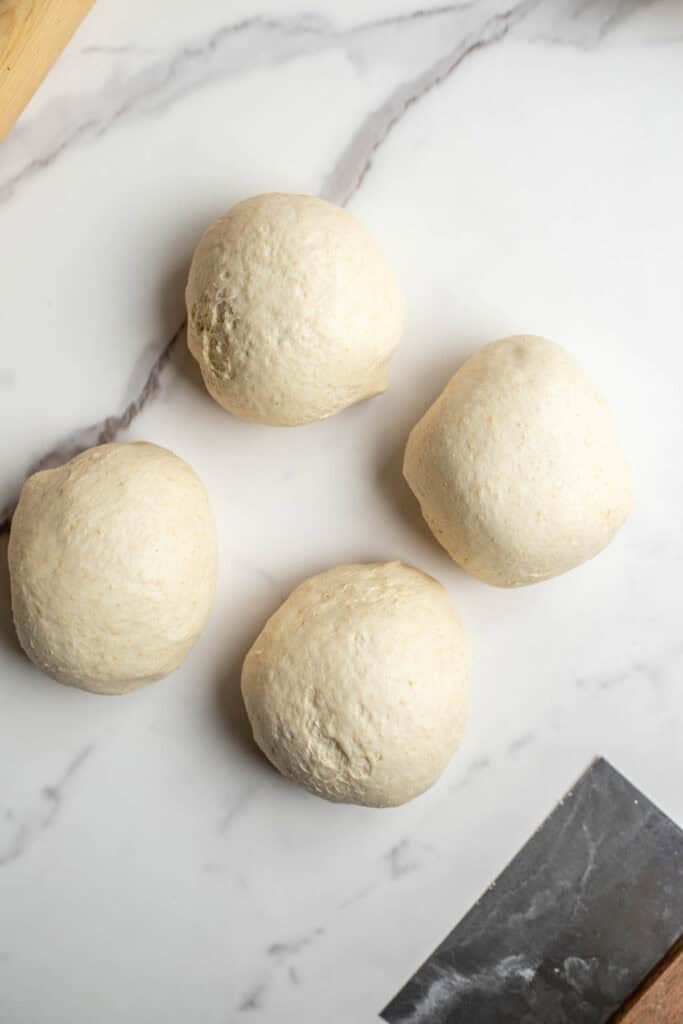 Sourdough balls cut into four equal pieces on a marble counter.