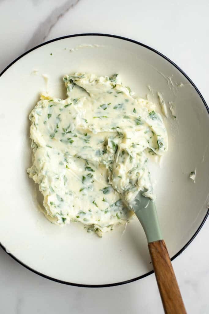 Fresh butter and herbs mixed together in a white bowl.