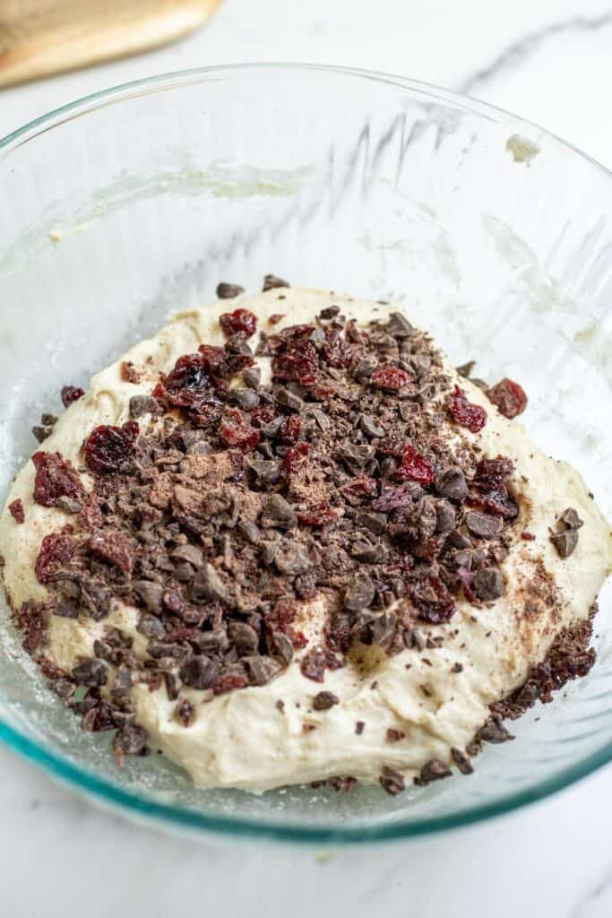 Chocolate chips and dried cherries added to a sourdough loaf in a mixing bowl.