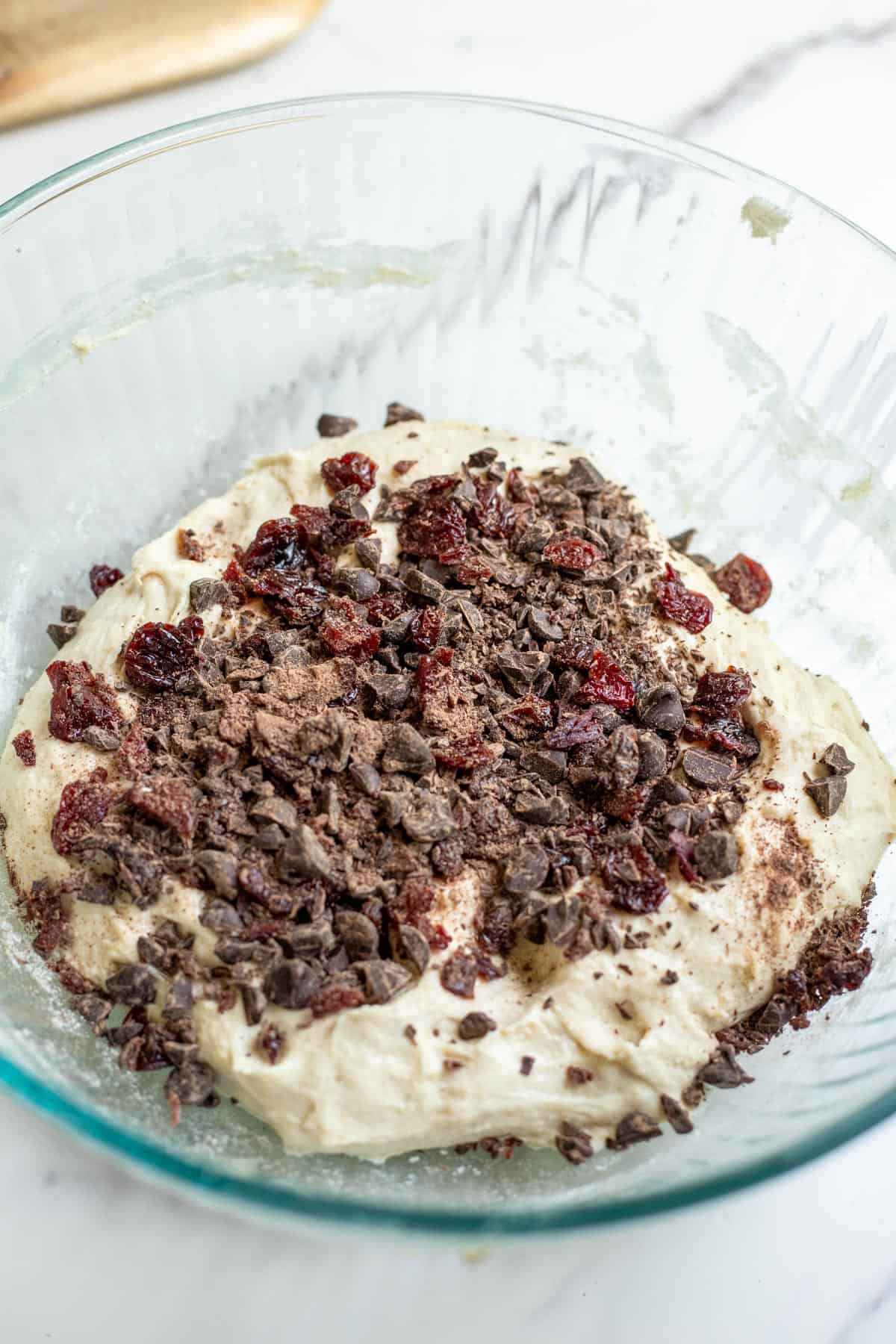 Chocolate chips and dried cherries added to a sourdough loaf in a mixing bowl.