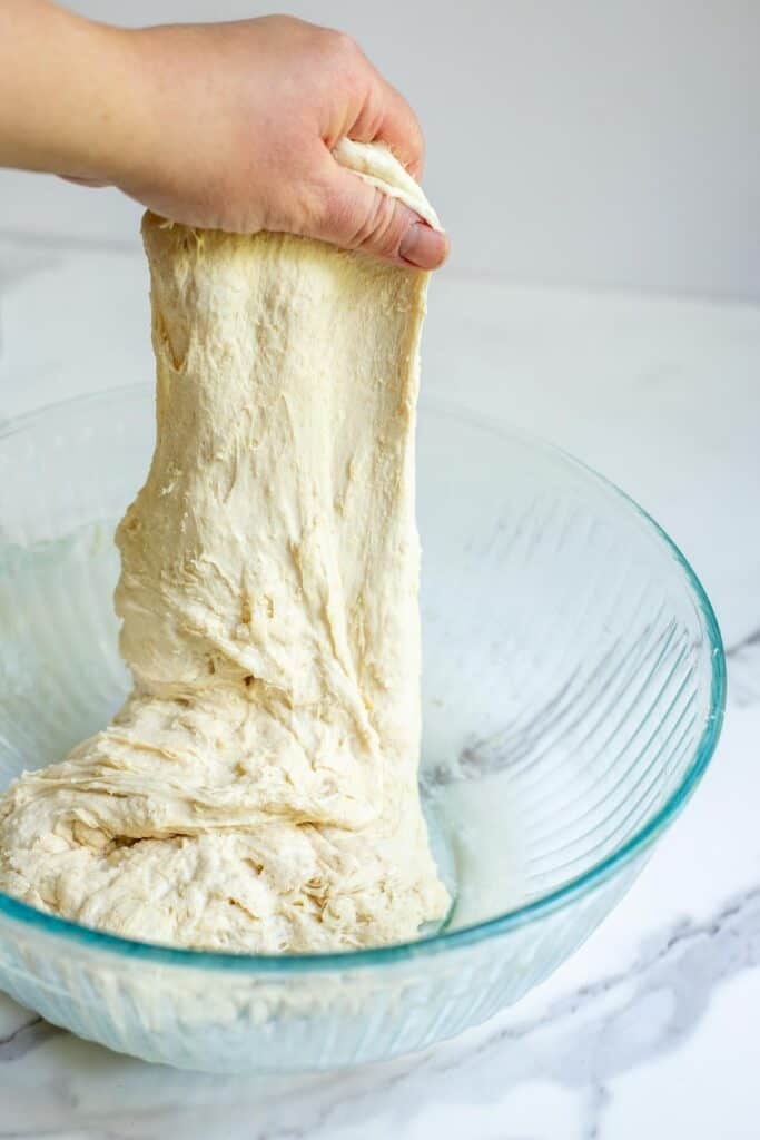 A hand pulling the dough upward from the bowl in a series of stretch and folds.