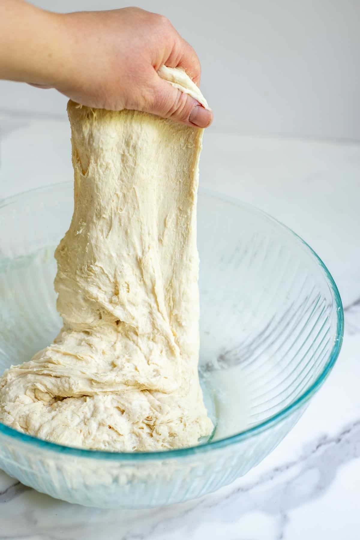 A hand pulling the dough upward from the bowl in a series of stretch and folds.