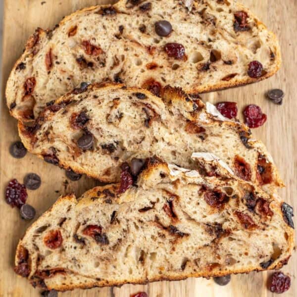a wooden cutting board with three slices of chocolate cherry sourdough bread.