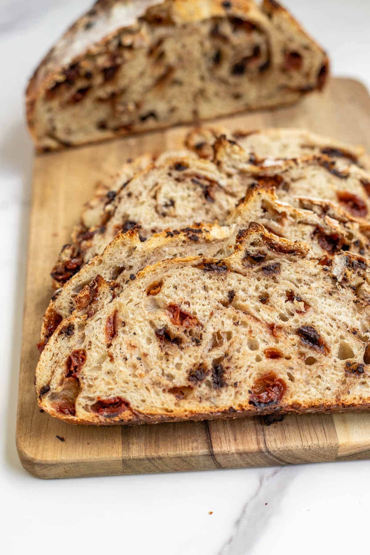 A chocolate cherry sourdough loaf of bread on a cutting board sliced in half.
