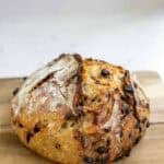 a sourdough boule with chocolate and cherries sitting on a wooden cutting board to cool.