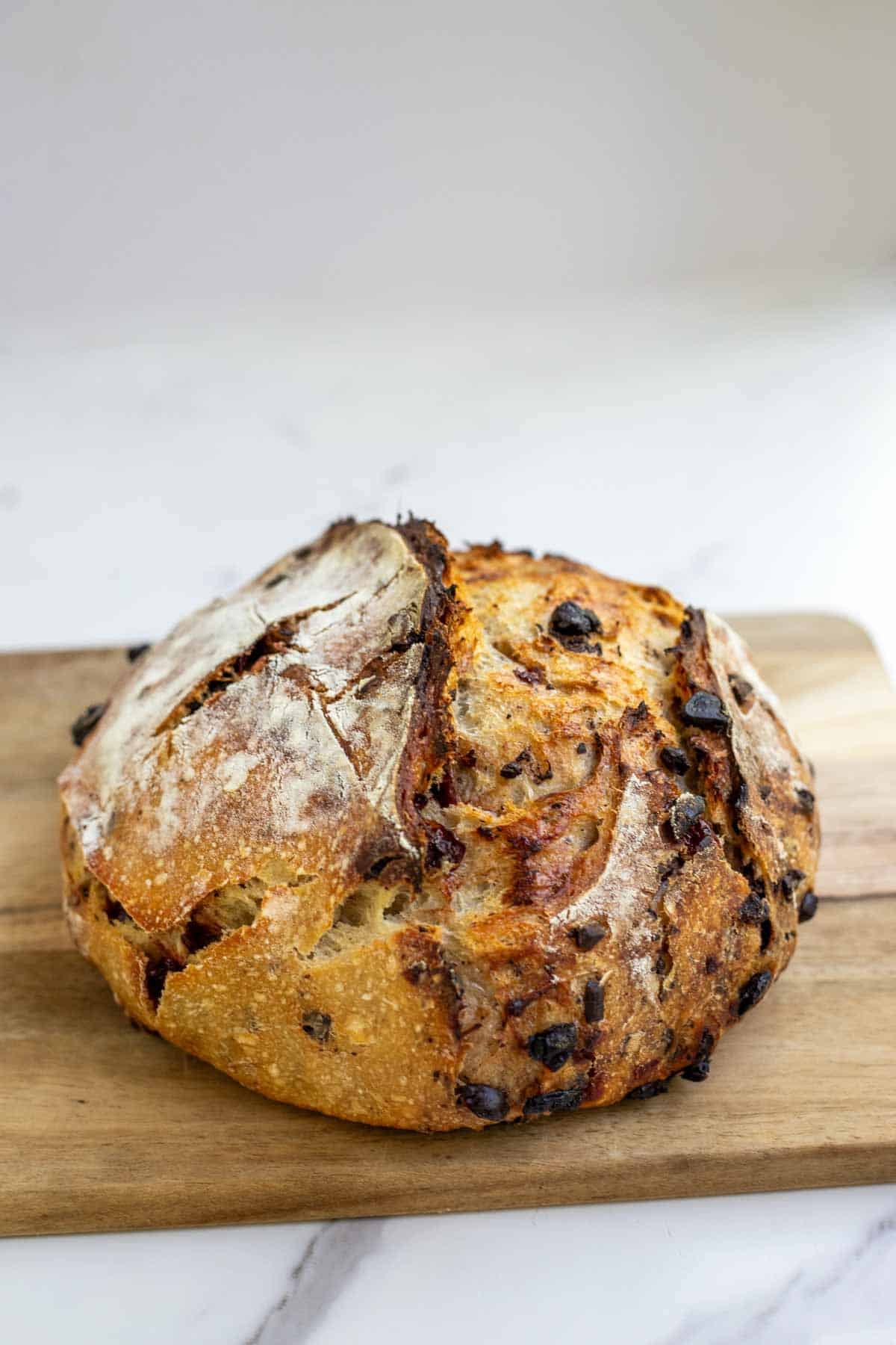 A sourdough boule with chocolate and cherries sitting on a wooden cutting board to cool.