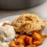 sourdough peach cobbler on a white dessert plate served with a scoop of ice cream.