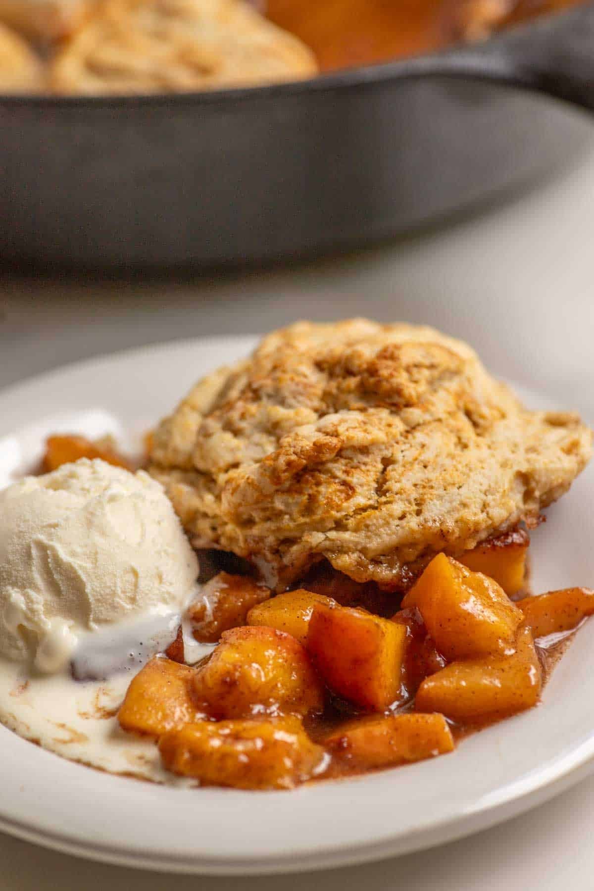 Sourdough peach cobbler on a white dessert plate served with a scoop of ice cream.