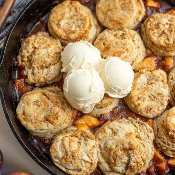 sourdough peach cobbler in a cast iron skillet with three scoops of vanilla ice cream on top.