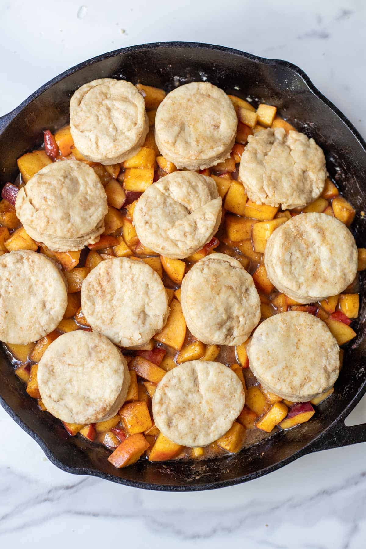 Uncooked biscuits placed on top of the peaches in a cast iron skillet.