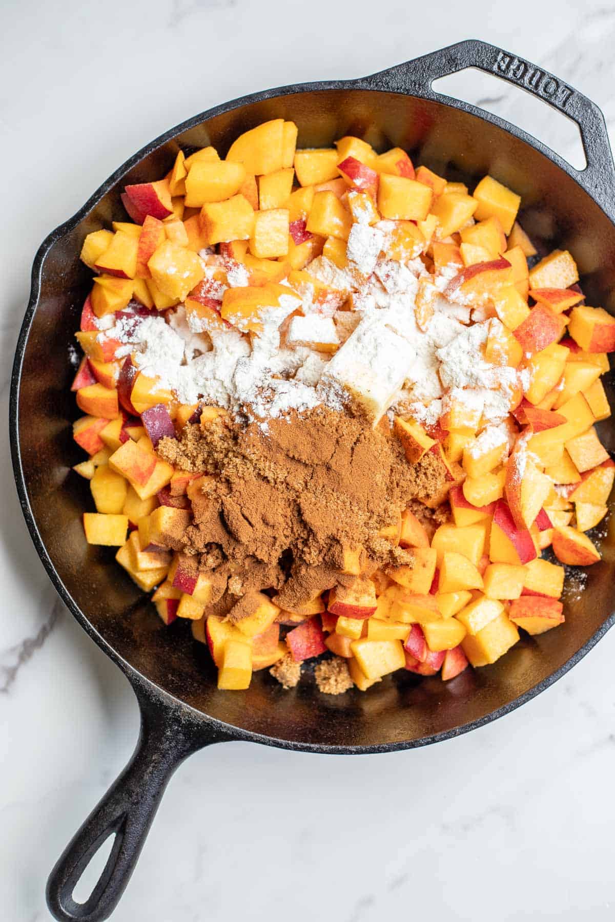 Chopped peaches in a cast iron skillet topped with brown sugar, butter, and flour.