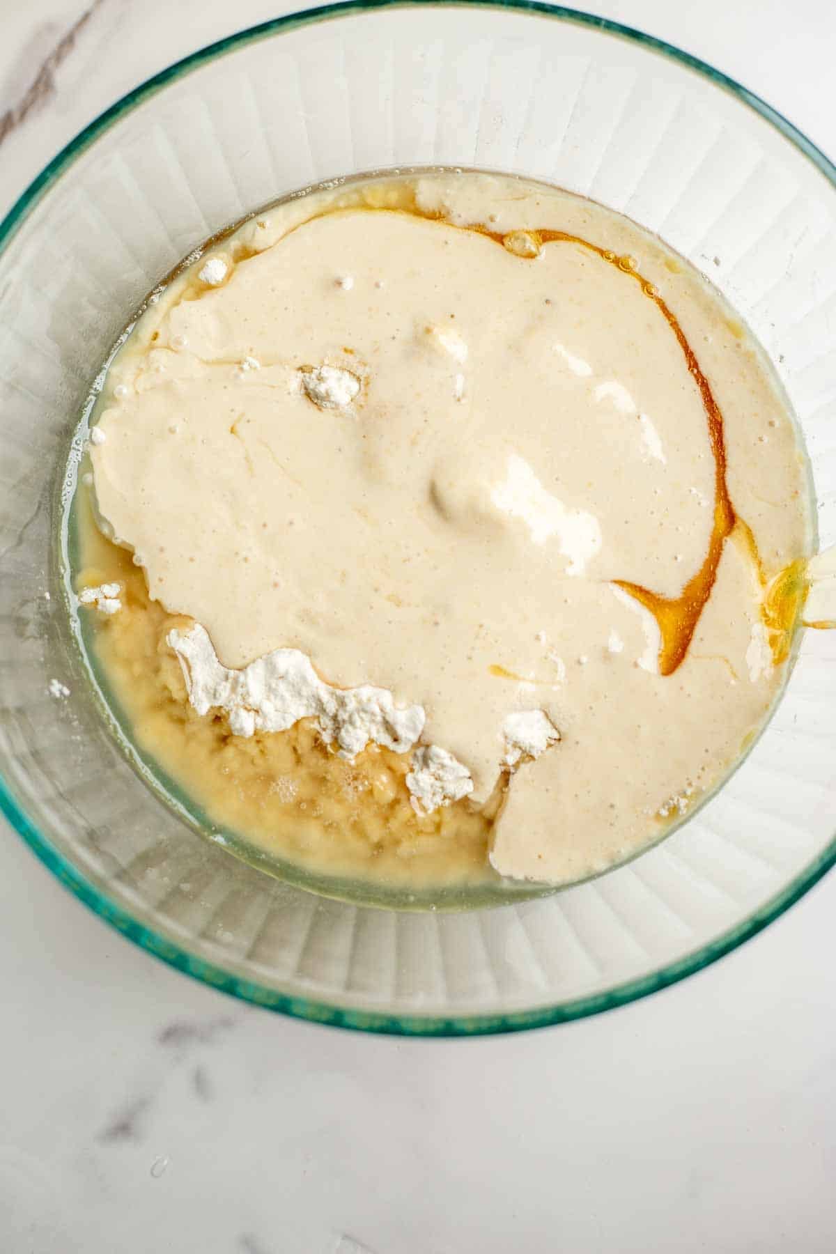 Flour, sourdough starter, honey, and coconut oil mixed together in a glass bowl.