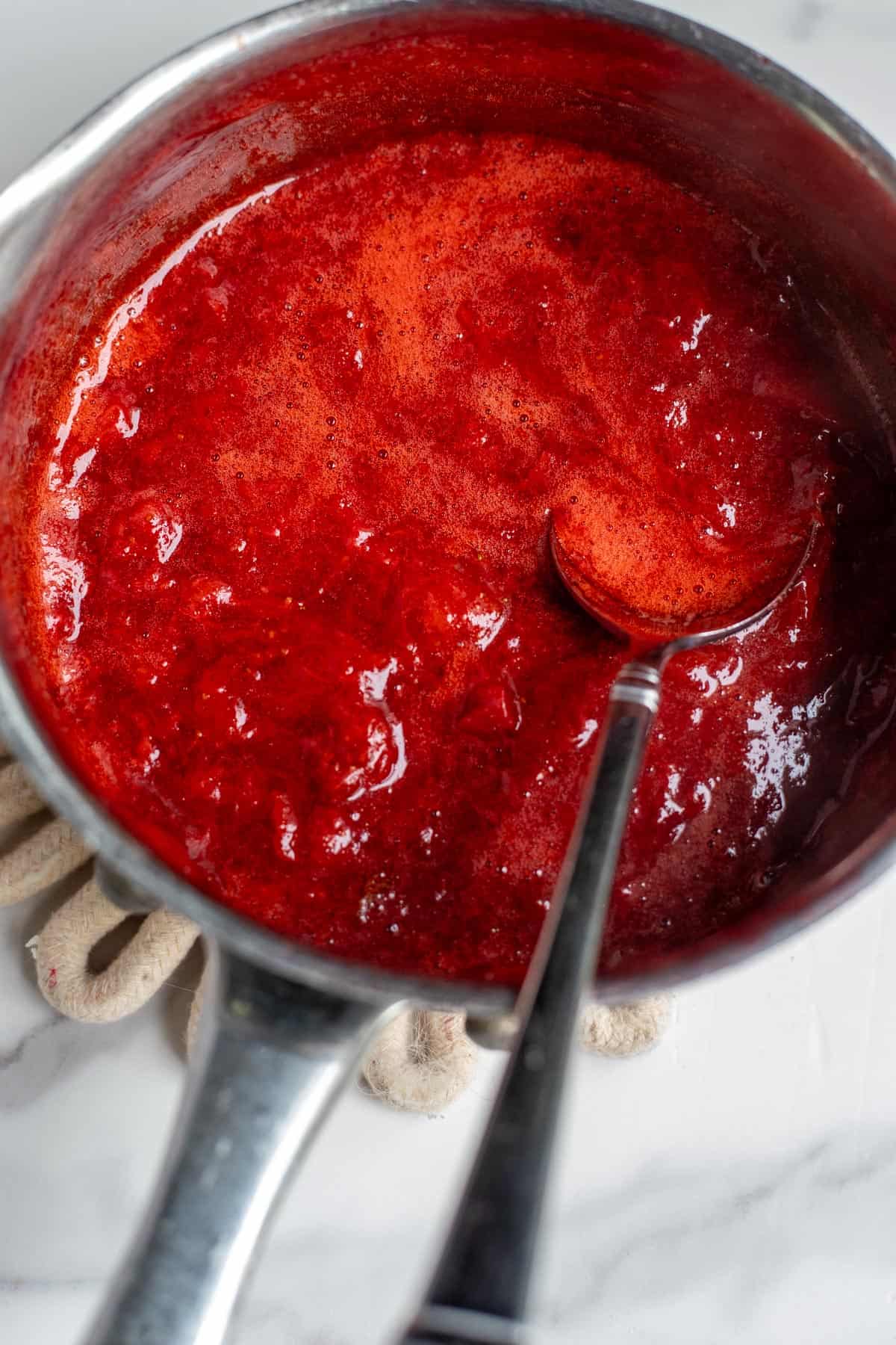 Strawberry sauce in a simmering pot with a serving spoon in the pot.