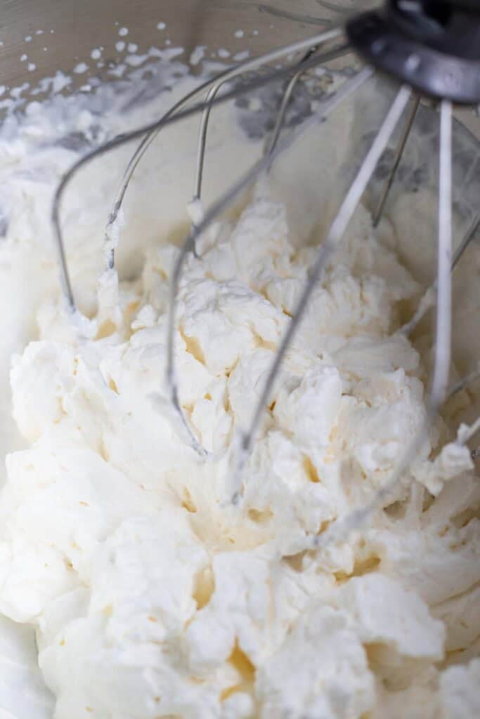 Heavy cream whipping together in a large metal mixing bowl.
