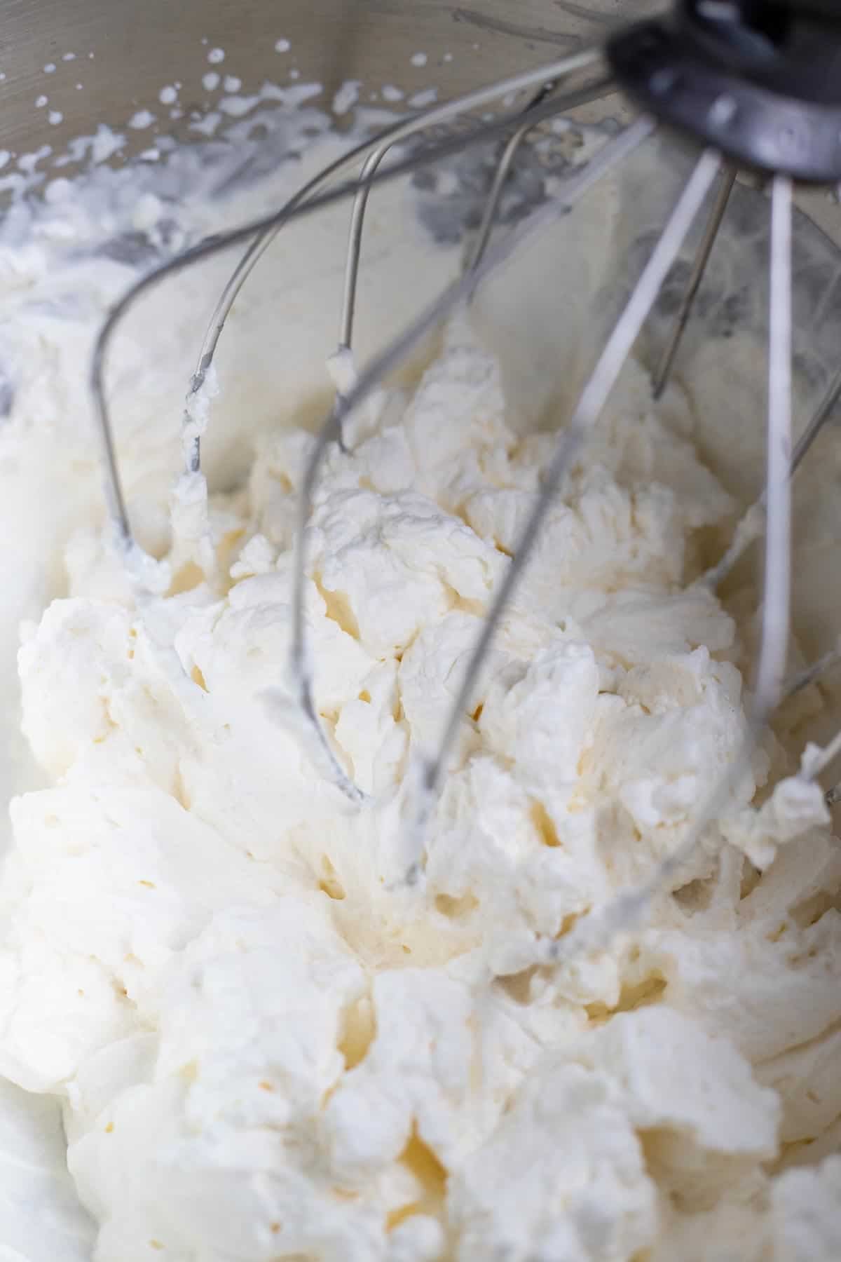 Heavy cream whipping together in a large metal mixing bowl.