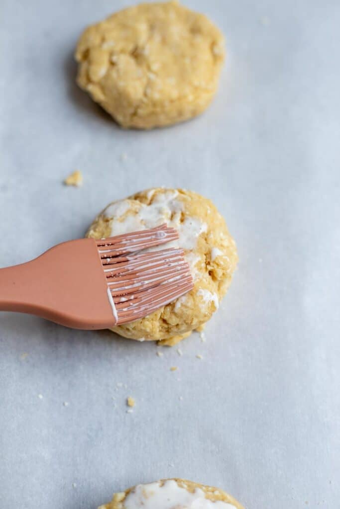 A pastry brush brushing heavy cream on top of a sourdough shortcake.