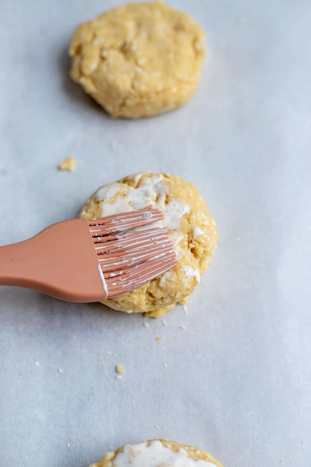 A pastry brush brushing heavy cream on top of a sourdough shortcake.