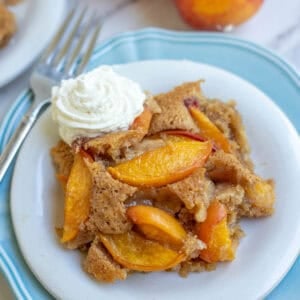 a white dessert plate filled with whole wheat peach cobbler topped with whipped cream.
